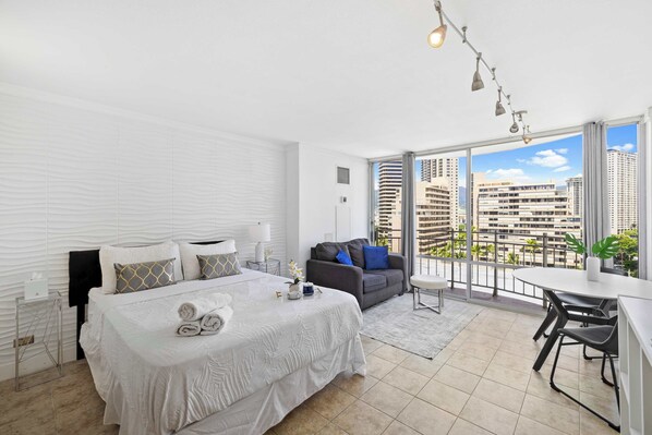 Bright studio with a queen bed, cozy sofa, and private balcony offering city views.