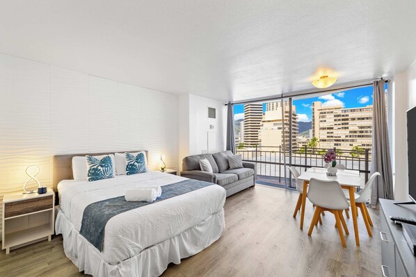Bright studio with a queen bed, cozy sofa, and private balcony offering city views.