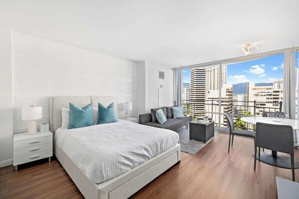 Bright studio with a queen bed, cozy sofa, and private balcony offering city views.