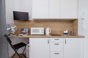 A kitchenette with white cabinets, a microwave, and a small dining setup with a chair and table.
