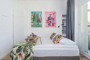 Another view of the bedroom, emphasizing vibrant wall art, white furniture, and balcony access.
