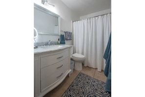 Bright bathroom with shower tub combo, large vanity and plenty of towels