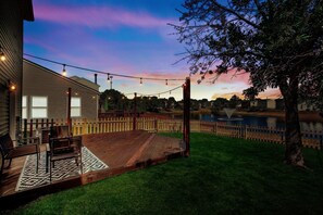 Fully fenced back yard with patio furniture, string lights and BBQ grill.