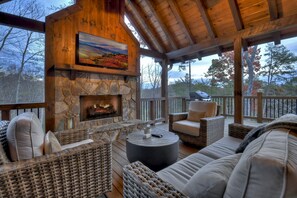 Relax on the cozy covered deck with a stone fireplace and serene forest views.