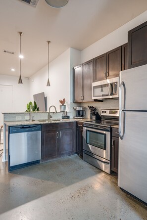 Fully stocked kitchen with basic cooking essentials, stainless steel appliances, granite countertops, and breakfast bar seating.