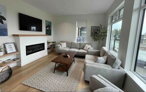 Cozy living room with fireplace, TV, games, and large windows.