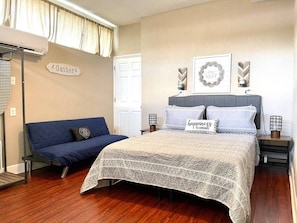 Queen bed, bedside tables with lamps, sofa, window with curtain, air conditioning, wall decorations, access door