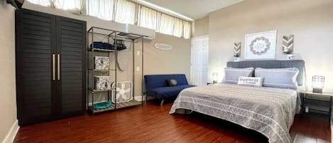 Room with queen bed, side tables with lamps, exterior windows with curtains, sofa, closet, hangers, fan, ironing table, iron, air conditioning, TV, and access door