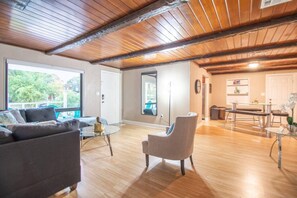 Living room with sofa and armchair, side table, window to the outside, lamp, mirror overlooking the dining room, main access door