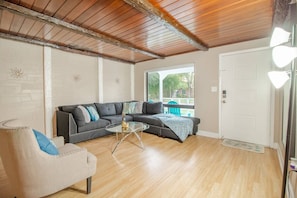 Living room with large sofa and armchair, side table, window to the outside, lamp and main access door