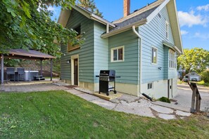 Private backyard features a 7 person hot tub under an all-weather awning, firepit with Adirondack lawn chairs, gas grill  and a hammock