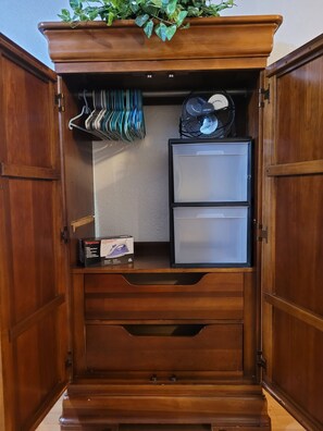 Armoire with hangers & drawers for clothing, an iron, and portable fan.