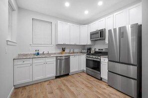 Navigate with ease in the spacious open plan kitchen, equipped with all essential cooking tools, pots and pans, and overhead cabinets filled with plates and glasses for your culinary endeavours.
