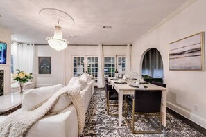 A stylish living room featuring a luxurious cloud sofa, seamlessly flowing into a sophisticated dining area that leads to an elegant cocktail lounge. Expansive doors open to a large patio, effortlessly extending the entertaining space outdoors and enhancing the overall sense of openness and connectivity.