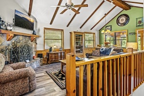Enter the cabin into the main living area with high ceilings, lots of comfortable furniture, a Smart TV, and a wood-burning fireplace.