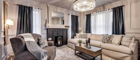 The spacious living room features a comfortable sofa and a cozy gas fireplace, perfect for relaxing. With chic style, a beautiful chandelier, and blackout curtains, the room is bright and inviting, offering a stylish space to unwind.