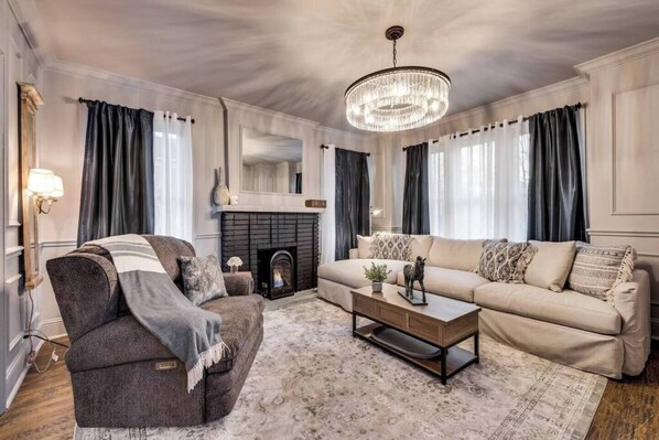 The spacious living room features a comfortable sofa and a cozy gas fireplace, perfect for relaxing. With chic style, a beautiful chandelier, and blackout curtains, the room is bright and inviting, offering a stylish space to unwind.