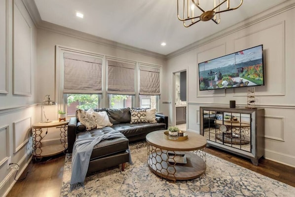The living room is a bright and inviting space, featuring a cozy leather sectional couch, a luxurious, and plenty of room to move around. The windows fill the room with ample light,  while a beautiful chandelier adds a touch of elegance and warmth to the atmosphere. 