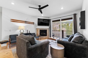 Living area featuring 2 sleeper sofas, mounted TV above a gas fireplace, and balcony access.