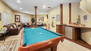 Enjoy relaxing in the basement living room, a dynamic space with three leather couches, a pool table, a 52-inch flat-screen TV, end tables, lamps, and a mini fridge.