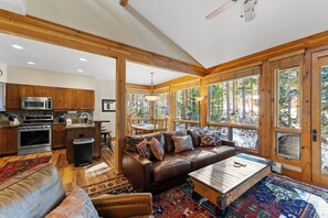 Main floor living area with fireplace, mounted flat screen TV, vaulted ceilings, and walls of windows.