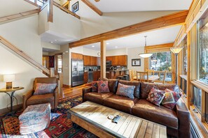 Main floor living area with fireplace, mounted flat screen TV, vaulted ceilings, and walls of windows.