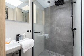 A bathroom with a glass shower enclosure, a sink, and a toilet, highlighted by gray tiles.
