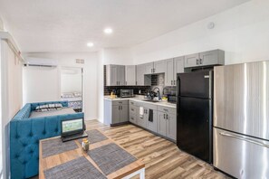 This shared room includes a kitchen with functional cabinets and a large refrigerator. It also features a small dining area.