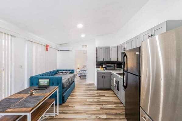 This shared room includes a kitchen with functional cabinets and a large refrigerator. It also features a small dining area.