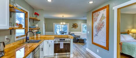 Explore our farmhouse-style kitchen with butcher block countertops and open shelving. Admire the Kodiak Island map as you cook on the stainless steel oven. View extends into bedroom and dining room, adding to the charm.