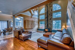 Come experience our spacious living room! Sink into the plush leather couch in our airy sanctuary, embraced by stunning vaulted ceilings and a rustic stone wall. Let the warmth of the wood stove envelop you in comfort.