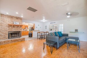 Living room with sofa and end tables, wall fireplace, dining room and access to kitchen