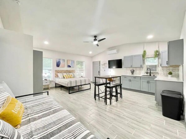 This unit features a comfortable bed, a fully-equipped kitchen, a dining area, a desk for work, a ceiling fan to keep the space cool, and a TV for entertainment. Everything is designed to provide comfort and functionality in one space.