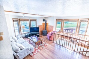 The inviting living area features three plush armchairs, a roomy couch, an electric fireplace, and soaring windows throughout the space.