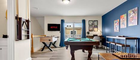 "The Game Room" features foosball, pool, wall-mounted connect 4, checkers, chess, dominoes, tic-tac-toe, a bar table with 3 stools, wall-mounted TV, slider leading to private balcony and a “work-from-home” desk