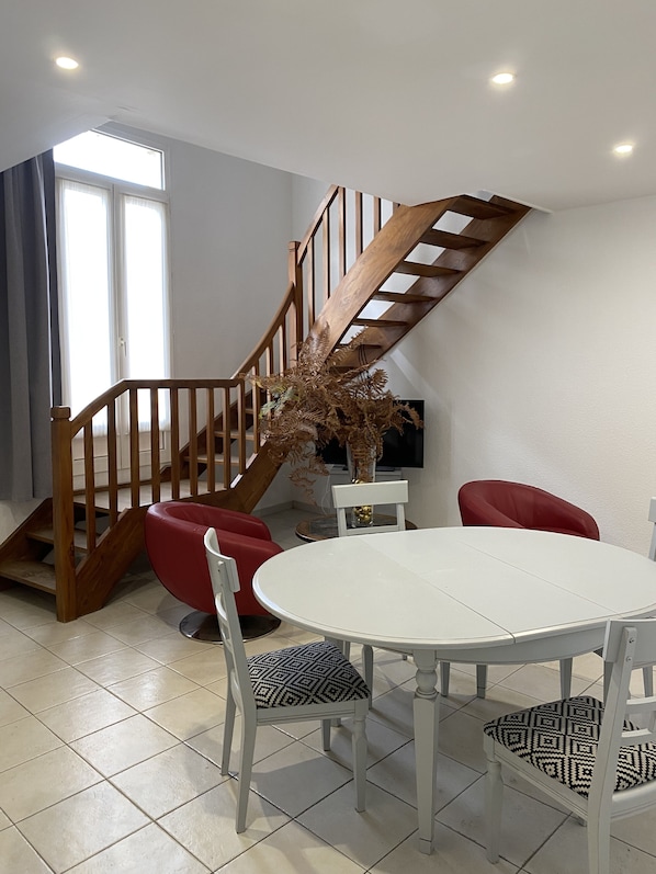 Pièce de vie, table, chaises, fauteuils, TV, meuble, escalier et fenêtre