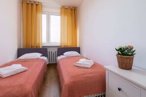 A bedroom with two single beds dressed in matching coral-colored linens, complemented by a potted plant.
