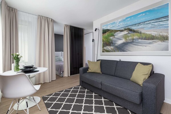 Modern living room with a cozy gray sofa, a coffee table, and large wall art depicting a beach scene.

