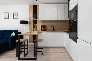 A compact kitchen with modern white cabinets, a black built-in oven, and a small dining area.
