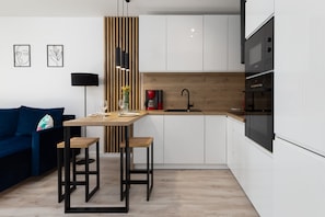 A compact kitchen with modern white cabinets, a black built-in oven, and a small dining area.
