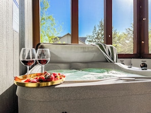 Unwind in the bubbling hot tub with a glass of wine and fresh strawberries, surrounded by serene natural beauty—your private oasis awaits.