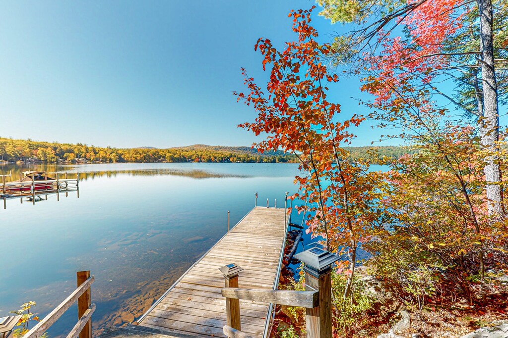 A long dock at a popular New Hampshire vacation rental has fall foliage growing near it on a bright, sunny day.