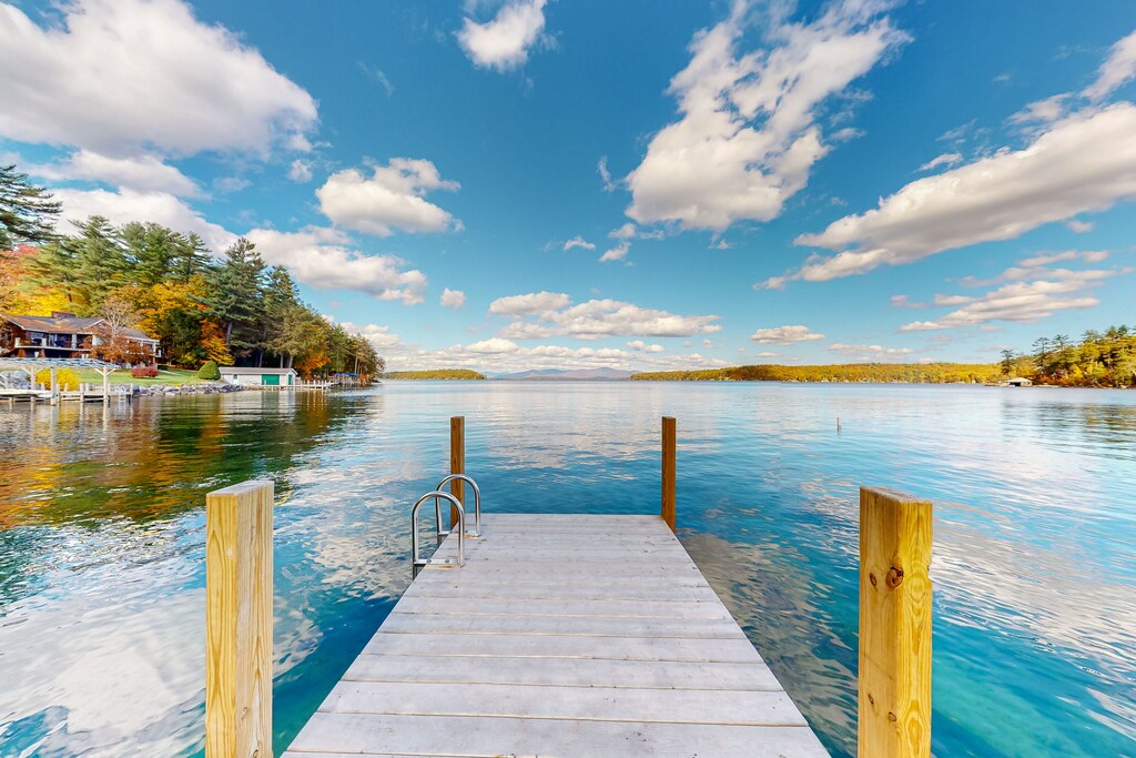 A private dock at a New Hampshire lakefront cottage for rent is seen on a sunny day with whispy white clouds in the sky.