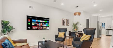 Living room with 65 inch smart TV and exposed brick.  Bright and airy view of the front windows and door.