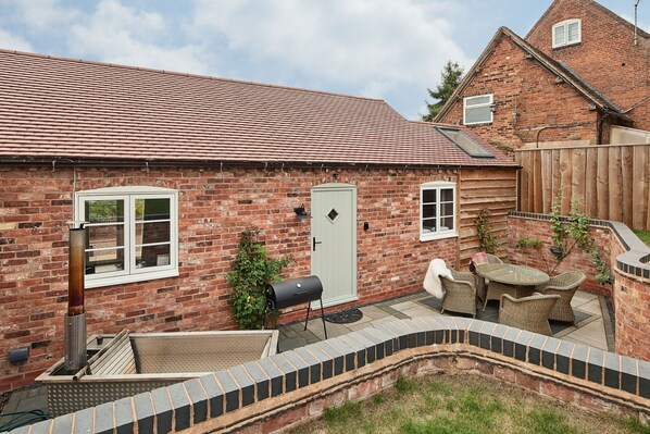 The private garden with a barbeque, rattan table and chairs and a wood-fired Swedish Hikki hot tub at Stable Cottage, Worcestershire