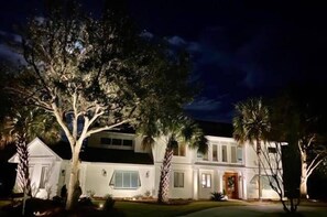 6 34th Avenue at night, welcoming visitors with uplit palm trees and landscaping.