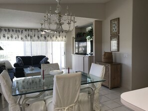 The dining area has a beautiful glass table,  chairs, and chandelier 