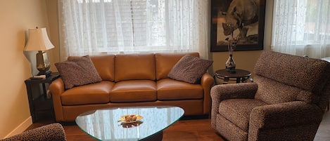 Living room area with a beautiful leather couch and two leopard recliners.