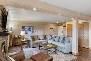 Living Room-This large, sectional couch pulls out to sleep 2. - Large Beige "L" shaped pull-out couch, brown leather armchair with ottoman, wooden coffee table