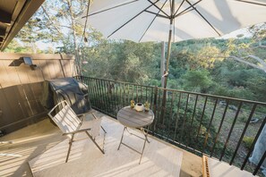 Sunlit patio with grill, cafe table, loungers, and forest view.